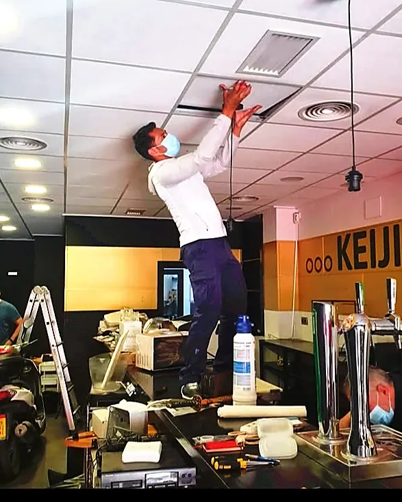 Técnico instalando conductos de climatización en el techo de un restaurante